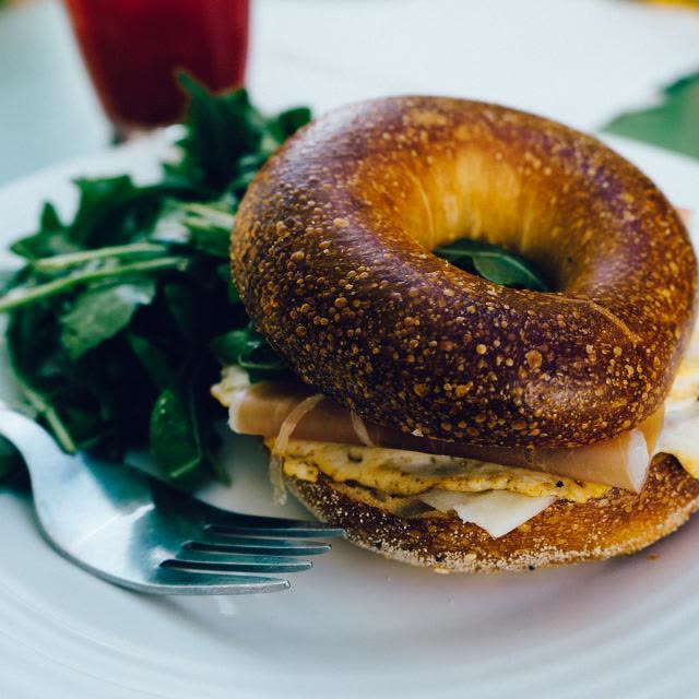 A bacon and egg roll on a plate with rocket