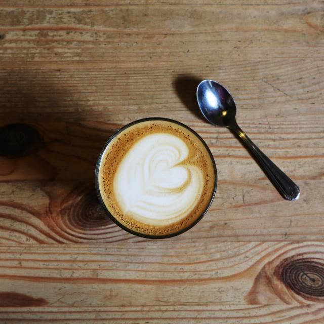 A flat white seen from above on a timber bench